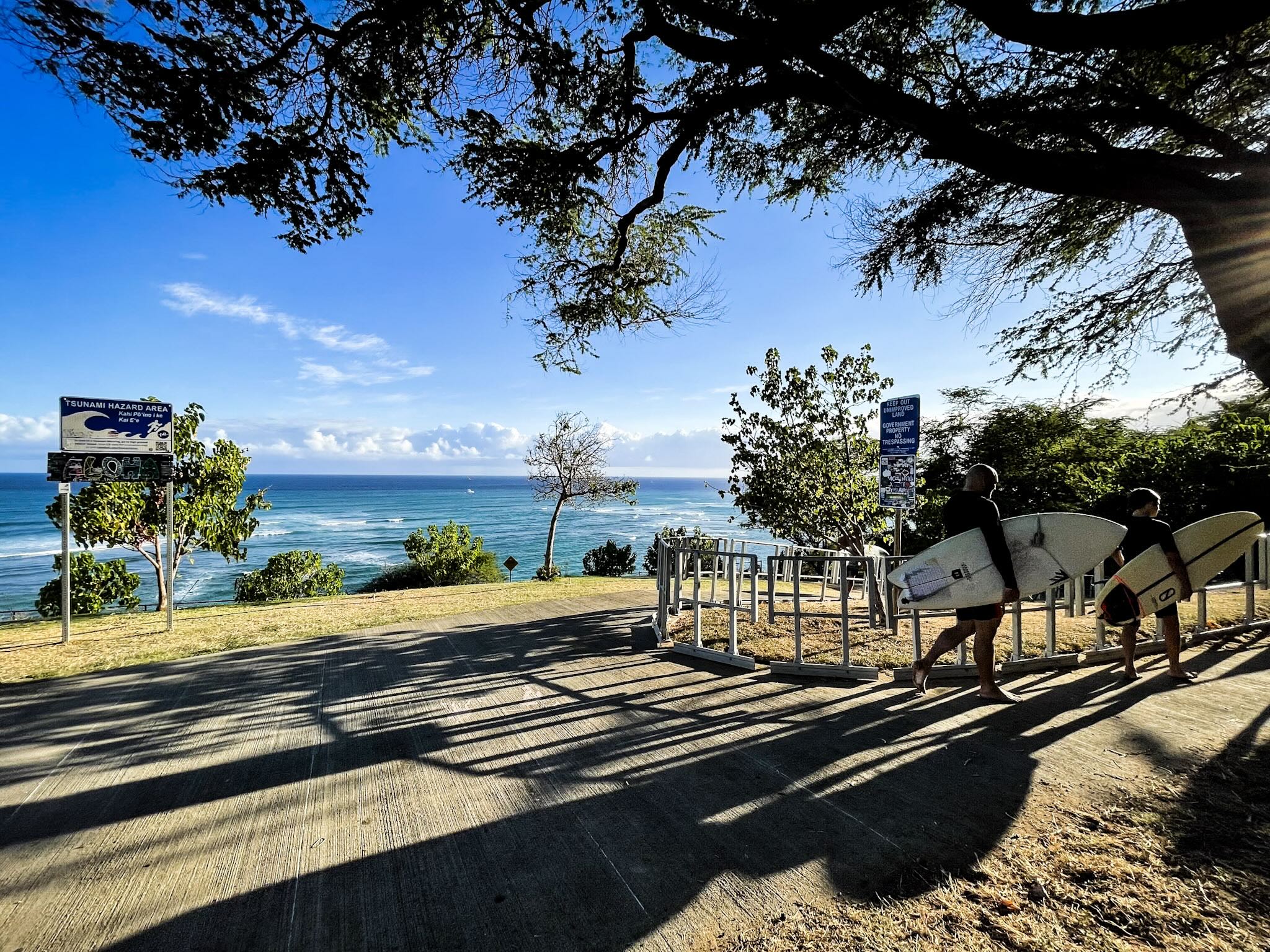 ダイヤモンドヘッド・ビーチ・パークで、西日を背にサーフボードを持って歩く地元サーファー