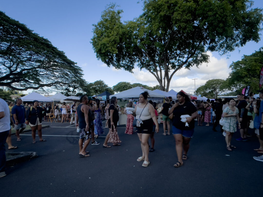 Kaneohe Farmers Market の会場を歩くローカルの人たち。エコバッグや屋台で買ったフードを手にしている。