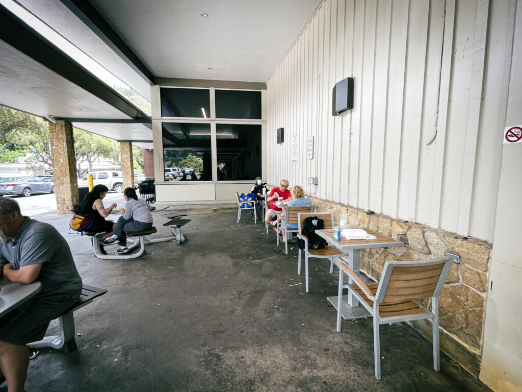 マノア・マーケットプレイスのテーブルでそれぞれ購入した食事を楽しむ人々