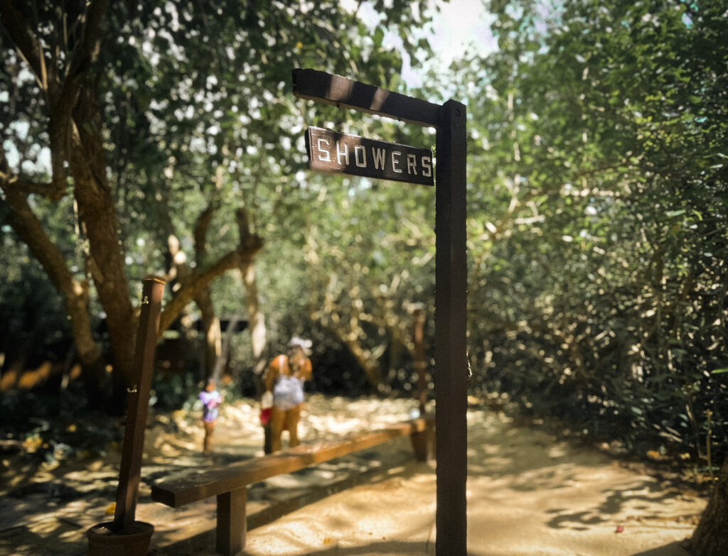 シークレットビーチの屋外シャワーで、子どもと一緒にシャワーを浴びる家族の後ろ姿